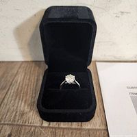Front view of 10K white gold moissanite engagement ring in black velvet box, showing round sparkling center stone and band.