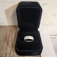 Ring displayed in open black velvet presentation box showing top view of textured band.