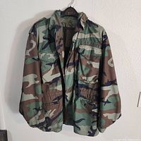 Front view of dark green US Army woodland camouflage jacket with chest marking and multiple pockets