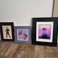 Three framed art prints leaning against a wall on wooden floor: Elvis Presley print, abstract geometric print, Historic Roseville water tower print