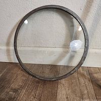Round glass boat porthole window leaning against a wall, showing front side of metal frame and clear glass.