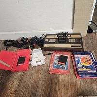 Full display of Intellivision console, two controllers, multiple game cartridges, and paper inserts on wooden floor.