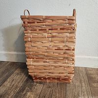 Front view of a stack of several rectangular woven wicker baskets with natural light brown and darker brown strips, with two handles on each basket.