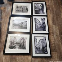 Top-down view of all six framed black and white print photographs laid on floor showing European city and canal scenes.