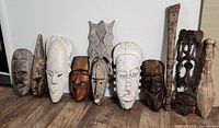Front view of 8 wooden tribal masks with various facial features and finishes
