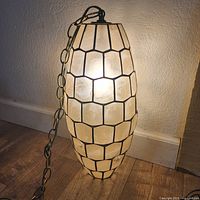 Side view of the elongated oval capiz shell hanging lamp lit, showing the geometric multi-sided design and brass frame with hanging chain.