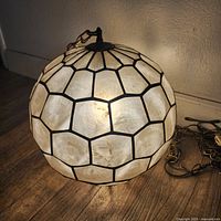 Spherical lamp illuminated on wooden floor showing capiz shell panels.