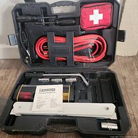 Open Michelin roadside emergency kit with all visible tools and items inside the molded black case showing jumper cables, first aid kit, white safety triangle, tire iron, and accessories.