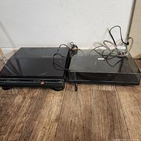 Two black vinyl turntables side by side with dust covers closed, power cords visible