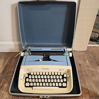 Blue Royal Aristocrat manual typewriter with cream-colored keys inside a hard blue carrying case, front view.