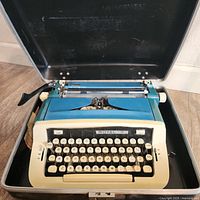 Royal Custom III manual typewriter inside an open black hard carrying case, showing the teal and beige color scheme and keyboard with round white keys.