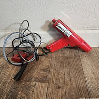 Red Snap-On timing light device and cables placed on wood floor adjacent to wall.
