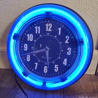 Front view of the Sterling & Noble clock illuminated with blue neon light, showing the clock face and neon tubing.
