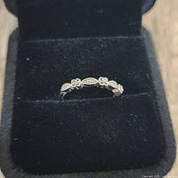 Close-up of sterling silver band ring with diamond and floral motifs inside a black velvet ring box.
