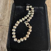 Close-up of the sterling silver bead necklace showing the lobster clasp and the shiny spherical beads on a black velvet surface.