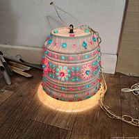 Front view of the illuminated hanging swag light showing the colorful floral patterns on the plastic shade and power cord plugged in.