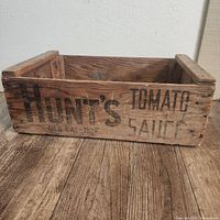Front side of the vintage wooden crate showing the branding 'Hunt's Tomato Sauce' in black letters on aged wood.