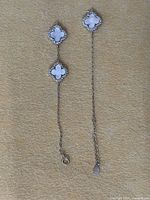 Full view showing two white clover charms connected by chain, broken at one end