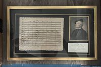 Full view of the framed memorabilia showing sheet music, portrait, and text plaque under glass in a gold frame.