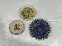 Three decorative plates on white surface, showing different designs and materials.