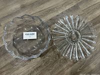 Two large clear glass bowls placed side by side on wood floor, showing floral shapes and scalloped edges.