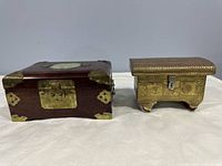 Photo showing front and side view of the wooden box with metal accents and the metal embossed box side by side on a white surface.