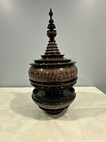 Full view of the black lacquered wooden bowl with detailed red and natural wood-tone patterns and its tall multi-tiered lid.