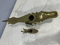 Two Indian metal oil lamps placed flat, showing their overall shape and intricacy, with the smaller lamp in front of the larger lamp.