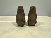 Front and back view of the two rustic brown earthenware bear sculptures placed side by side on a white cloth background. Both show Asian characters painted on their backs.