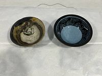 Lot displaying two rustic clay bowls side by side on a white surface showing the front and inner design.