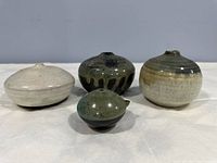 Front view of four small clay pottery pieces with varied glazes and shapes, displayed on white surface