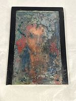 Front view of the framed abstract painting showing multicolor face design with a cracked texture on glass slides.