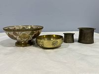 Four bronze metal decorative containers arranged in a row, showing varying sizes and styles including bowls and cylindrical containers.