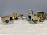 Front view of the full lot showing two ceramic bowls, four mugs, one teapot, and one decorative pot, all with hand-painted bird and floral designs in multiple colors