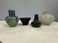 Four vintage marbled decorative vessels displayed on white surface; three glass vases in multicolor patterns and one ceramic lidded bowl with embossed flowers.