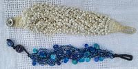 Photo showing both bracelets side by side, cream crochet with white beads bracelet on top and black crochet with blue beads bracelet below.