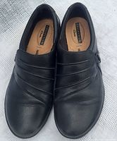 Top view of black leather slip-on shoes labeled Clarks Collection showing pleated front detail and cushioned insole.