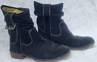 Side view of both black suede Fly London boots showing round toe, buckle strap detail, stitching, and short heel