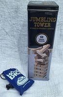 Metal tin for Jumbling Tower game with image of wooden blocks and blue Math Dice pouch alongside