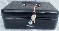 Closed view of black Garrison cash box showing the handle on top, front lock and attached two keys.