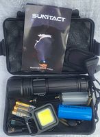 Kit contents including flashlight, batteries, charger, LED panel light, wrist strap, and user manual inside black foam-padded carrying case.