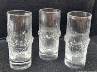 Three clear glass shot glasses standing upright showing textured bark-like pattern characteristic of Iittala Niva series by Tapio Wirkkala.