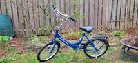Side view of the blue Schwinn folding bike showing brand name, folding hinge, saddle, front and rear fenders.