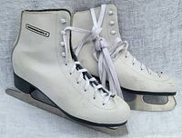 Pair of white Winnwell figure skates with laces and metal blades on a light surface.