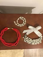 Overview of three necklaces: red multi-strand bead, white bead with ribbon, and crystal floral necklace