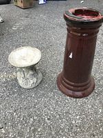 Small concrete bird bath basin and tall brown ceramic pedestal stand damaged at top with missing plate, shown on pavement.
