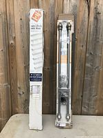 Two boxed items: white mini blinds in a long narrow box, and an adjustable metal drapery rod with ornamental finials in plastic packaging.