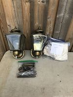 Two brass wall lantern lamps resting on a surface next to a bag containing extra glass panes and screws.