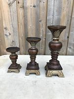 Front view of the set of three wooden candle holders with metal detailing on a table against a wood panel background