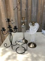 Black metal candelabra, two brass and glass candle holders, glass holder wrapped in bubble wrap, and a small glass and metal holder on a table